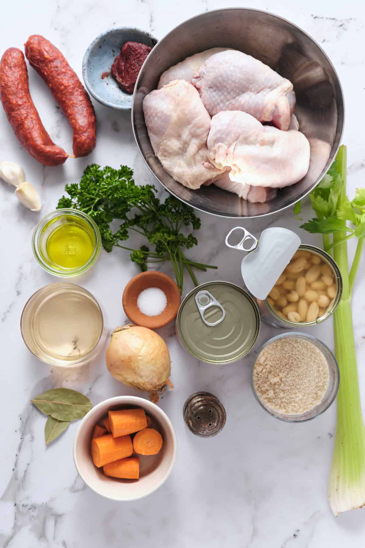 Sliced raw chicken thighs with vegetables and seasonings for healthy homemade soup or stew. Fresh herbs, carrots, garlic, beans, and spices are prepared for nutritious meal prep or cooking.