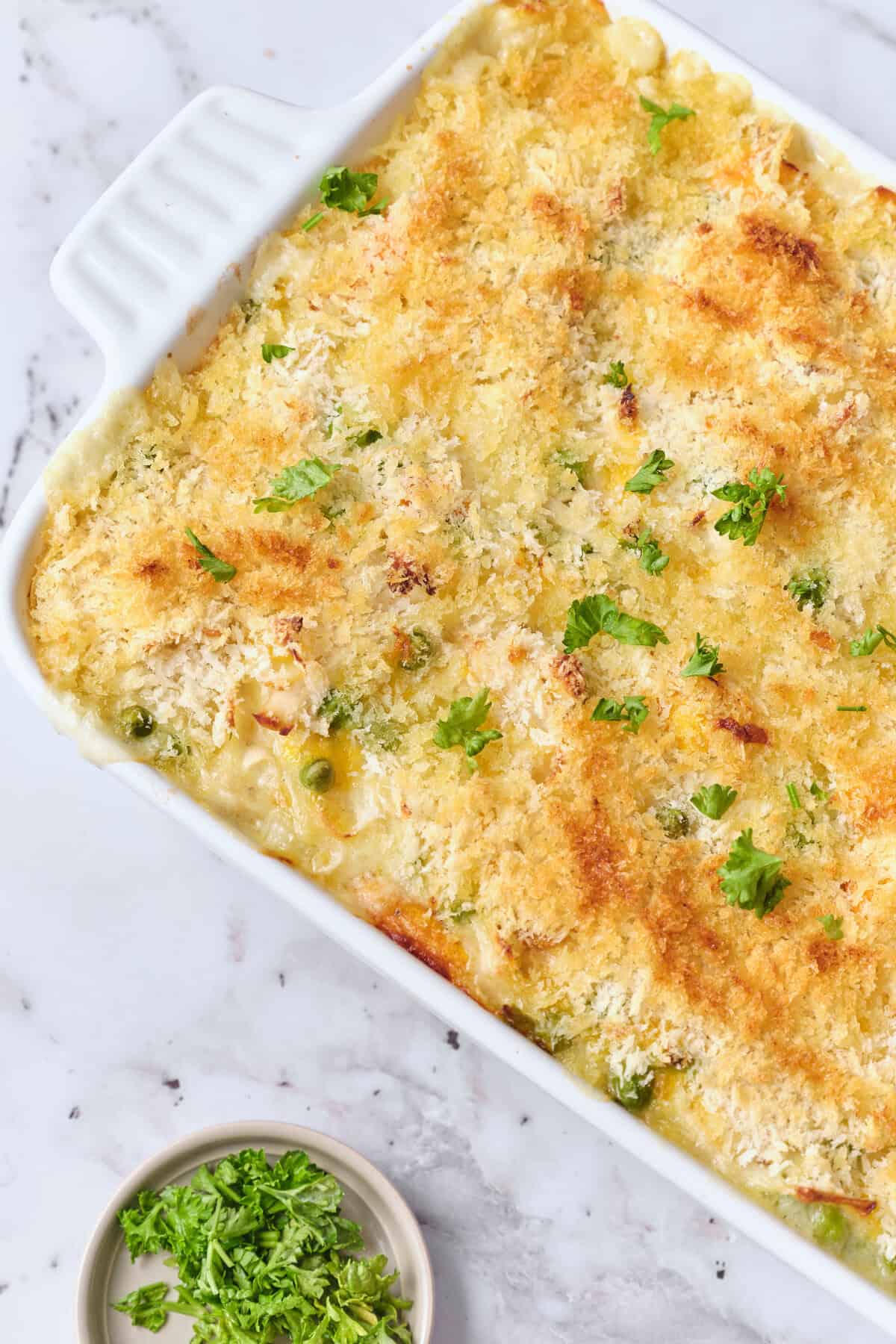 Cheesy baked casserole with breadcrumbs, peas, and fresh herbs in a white baking dish, healthy comfort food, perfect for family dinners or meal prep, high in protein and vitamins, delicious and easy to make.