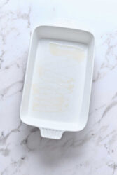 Empty white baking dish with a small amount of melted butter or oil, on a marble countertop, ready for healthy cooking or baking, promoting clean eating and nutritious recipes from Food Faith Fitness.
