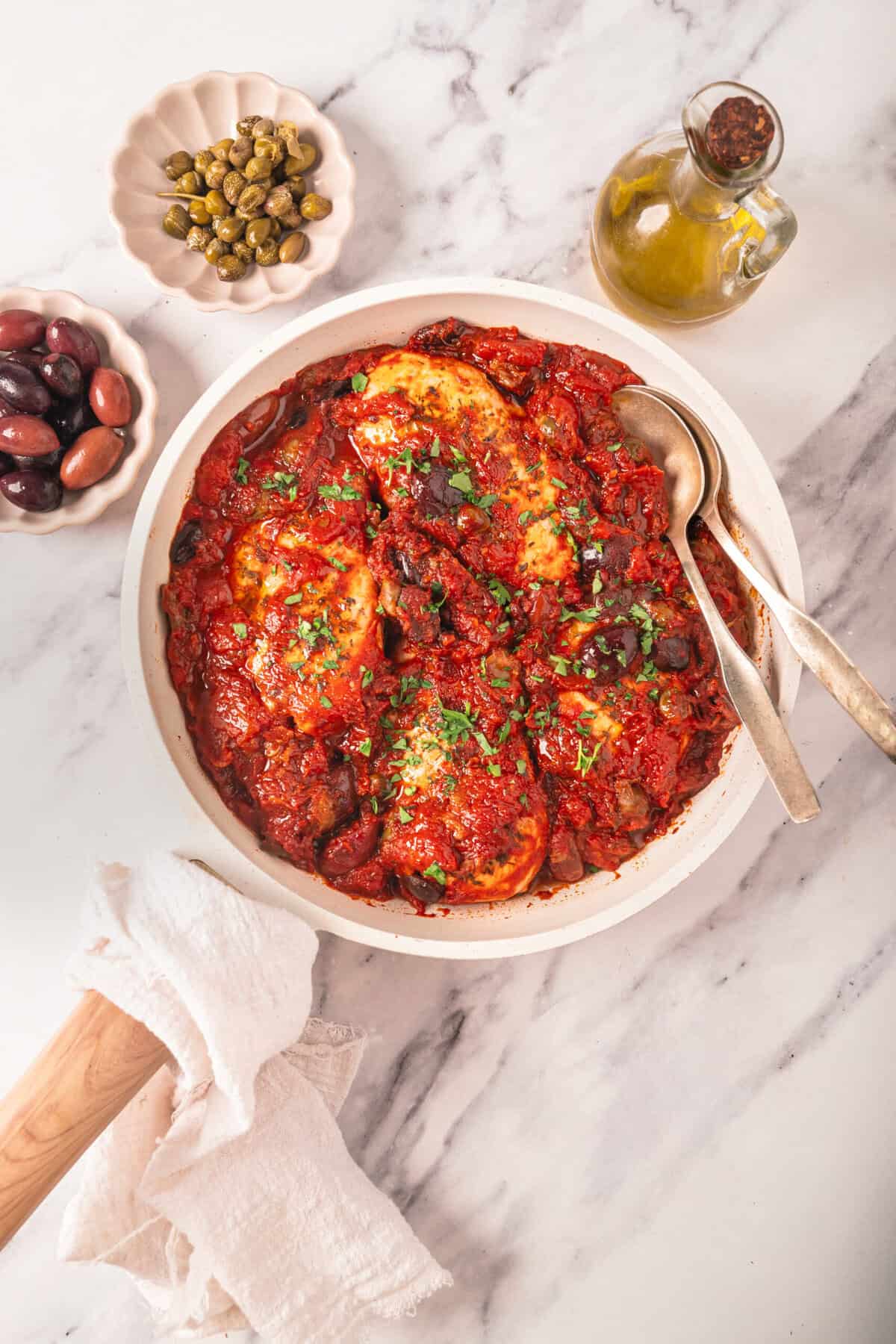 Rich and savory shakshuka with poached eggs in tomato sauce, served with black olives, capers, and olive oil, on a white marble surface, healthy breakfast or brunch option, food faith fitness.