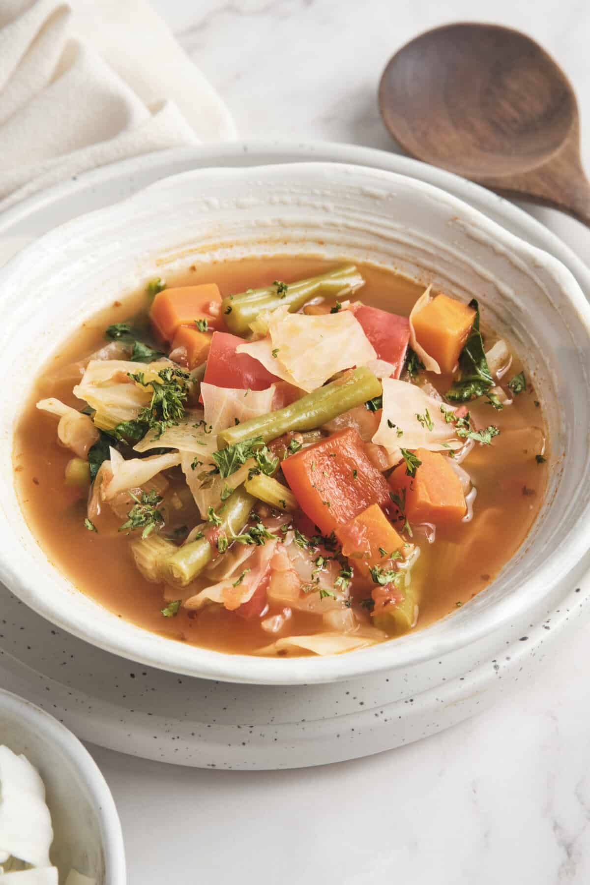 Vegetable soup with carrots, celery and cabbage in a white bowl, healthy and nourishing food with fresh ingredients.