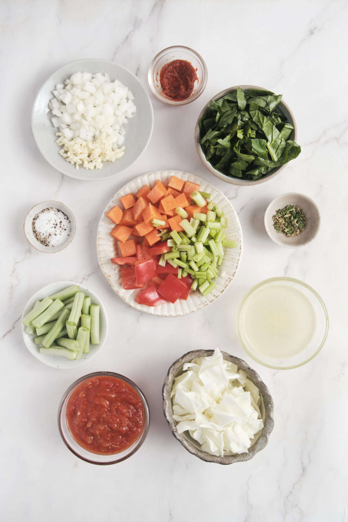Chopped vegetables and spices for healthy food preparation, including onion, celery, tomatoes, spinach and spinning, arranged on a white marble surface for a nutritious recipe.