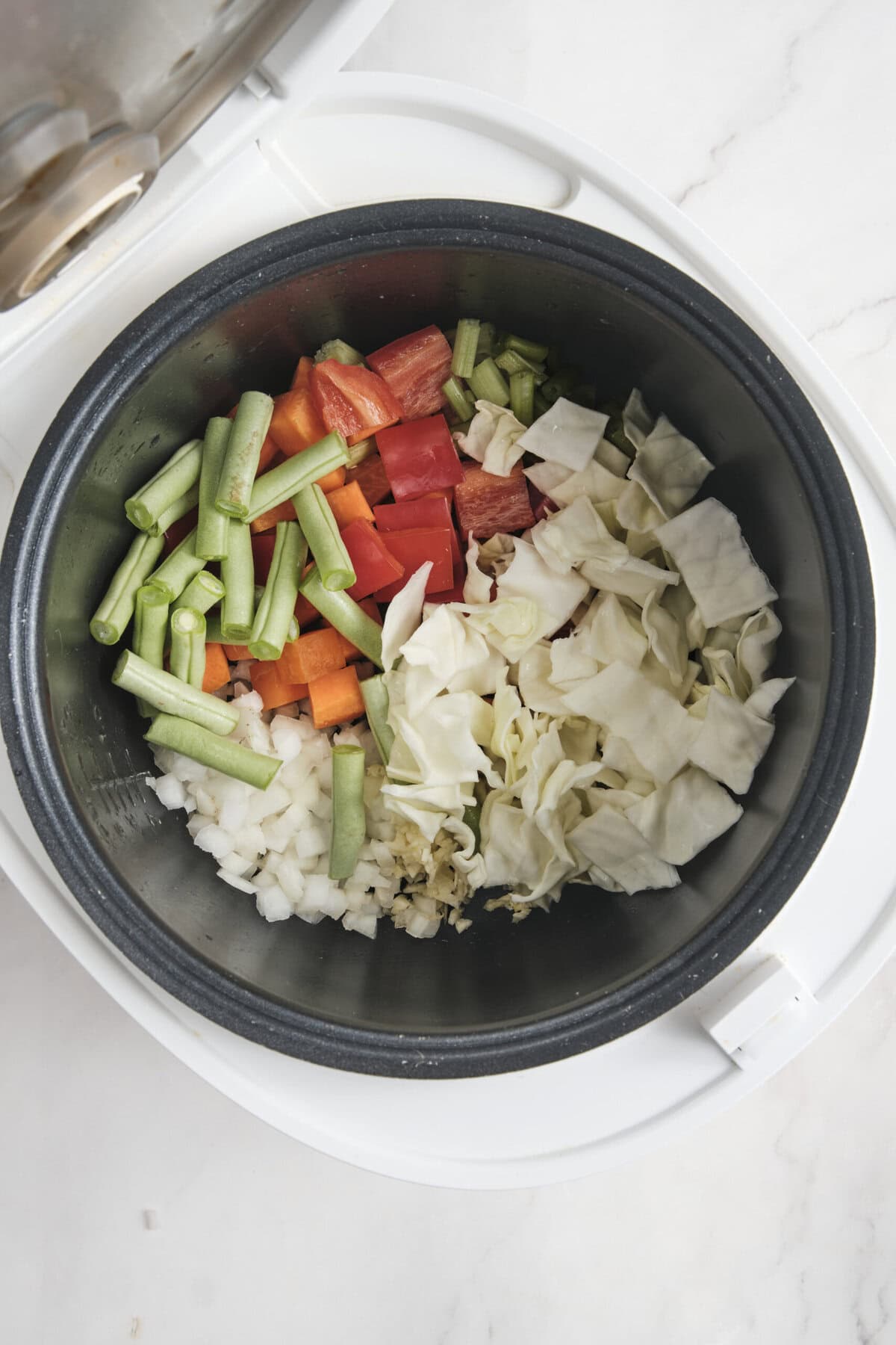 Vegetables in a slow cooker, including chopped cabbage, carrots, celery, bell peppers, onion, and garlic; healthy meal prep for nutritious recipes.