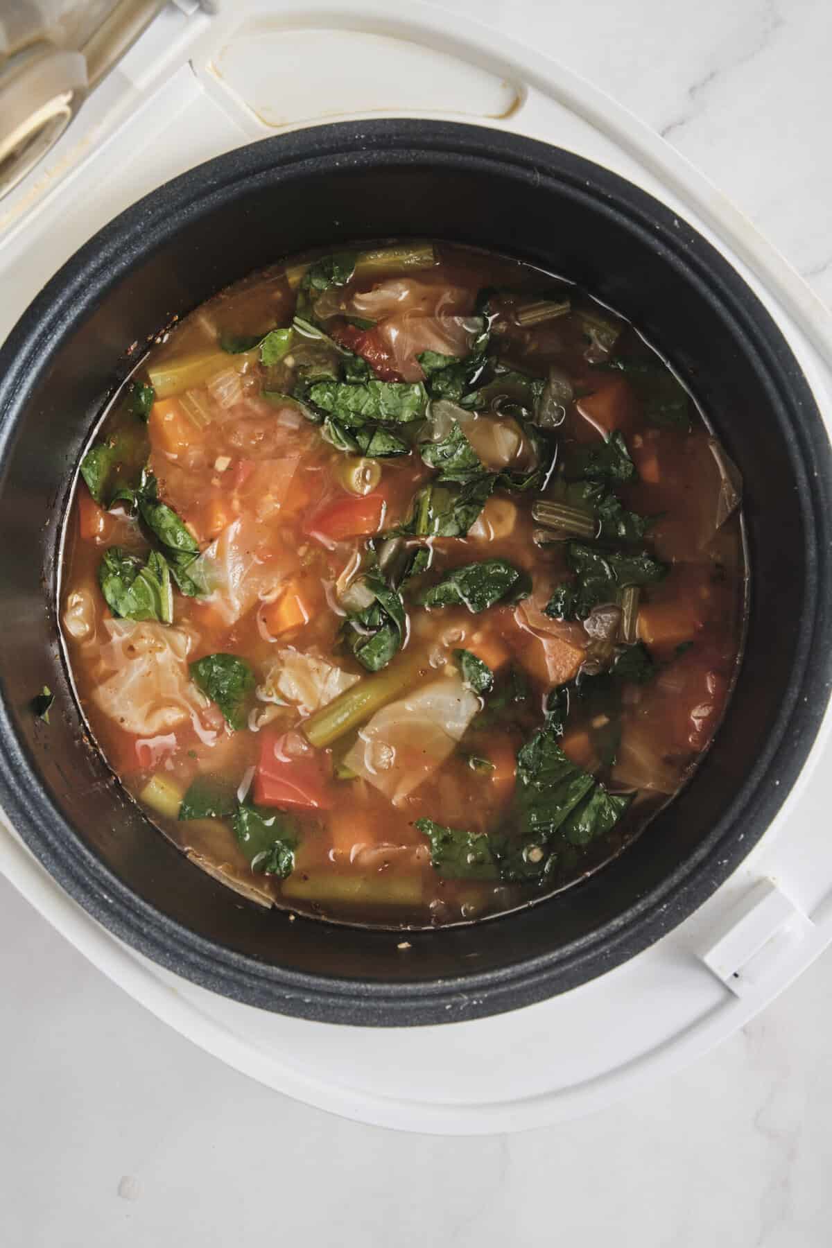 Steamed vegetable soup in a rice cooker featuring fresh greens, carrots, and tomatoes, perfect for healthy, nutritious meals aligned with Food Faith Fitness dietary tips.