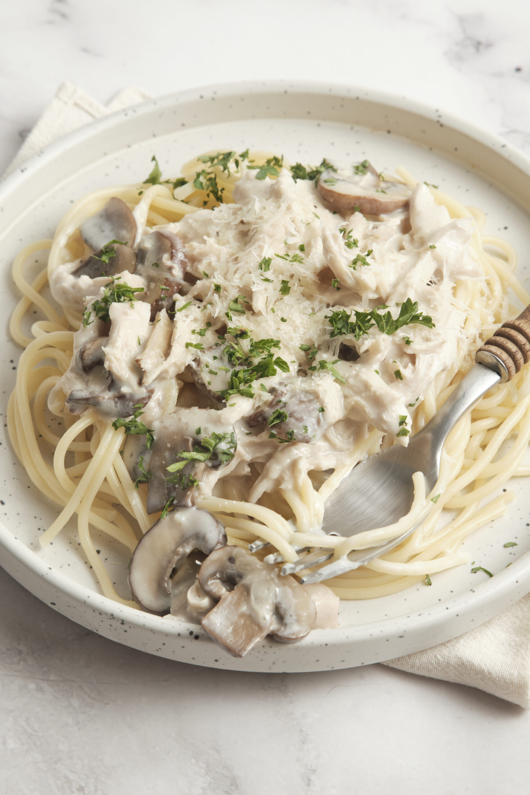 Creamy mushroom chicken pasta in a white sauce topped with fresh herbs, served on a white plate for a healthy and delicious meal. Perfect quick dinner idea for mushroom lovers.
