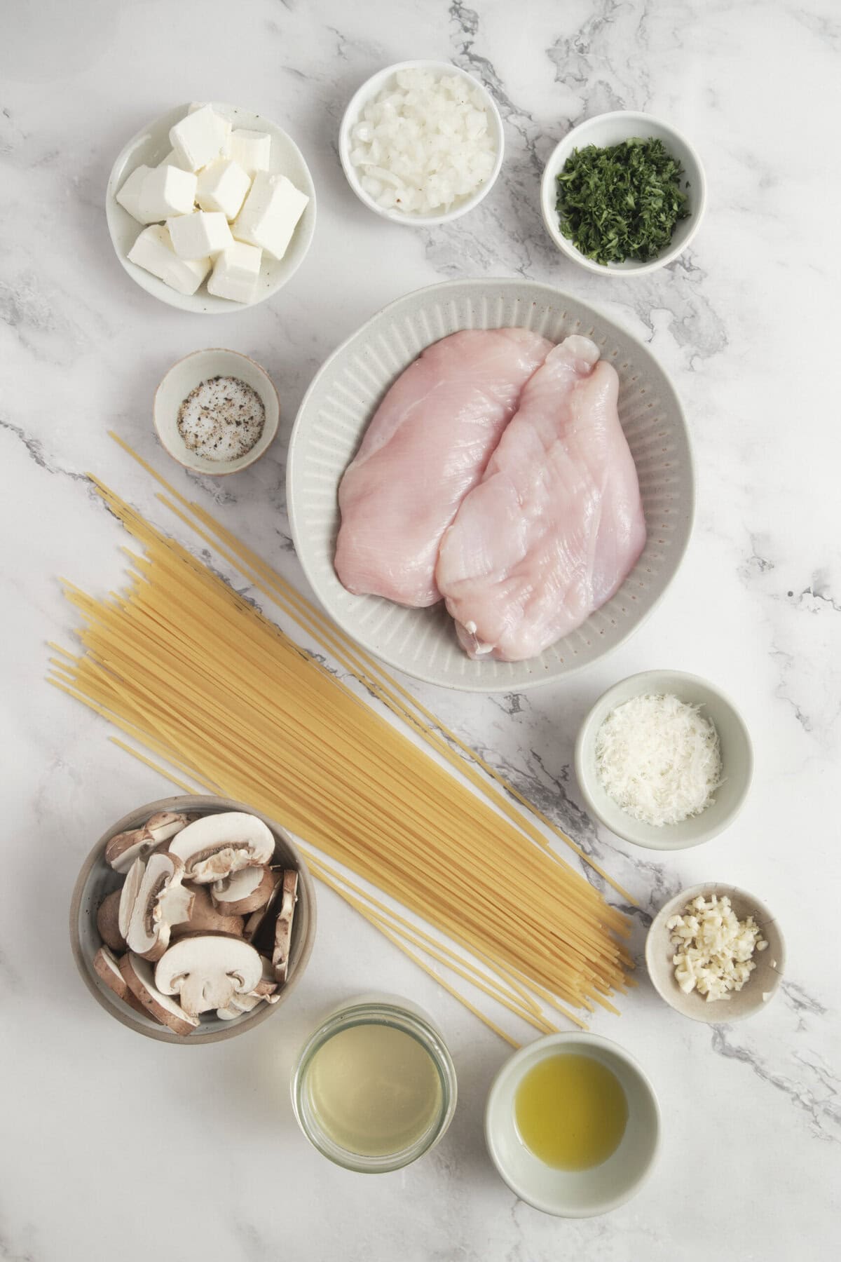Fresh chicken breasts, pasta, mushrooms, chopped onions, spinach, garlic, cheese, and seasonings on a marble surface, highlighting healthy meal prepping and easy dinner recipes from Food Faith Fitness.