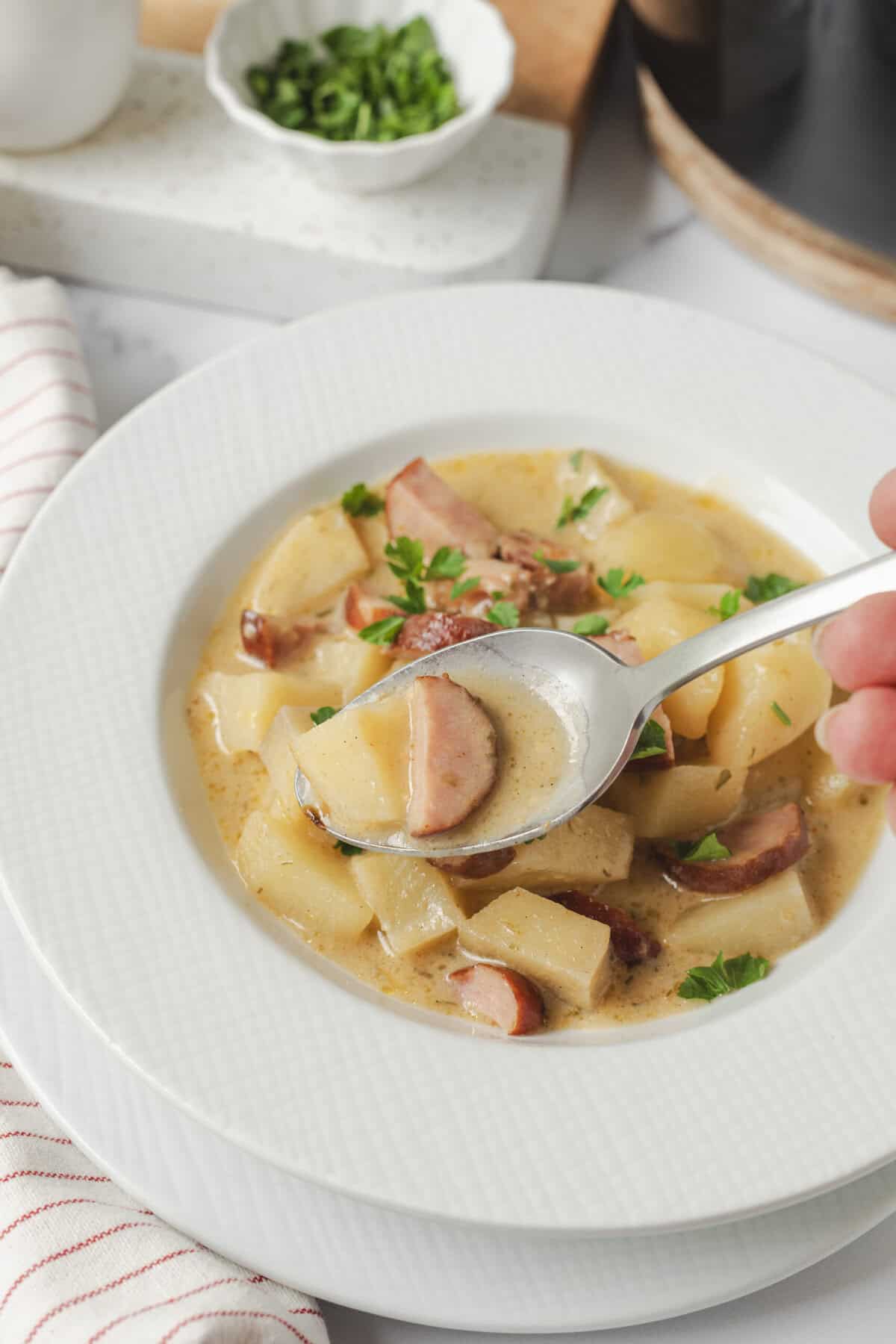 Creamy potato soup with bacon, garnished with fresh parsley in a white bowl on a kitchen countertop.