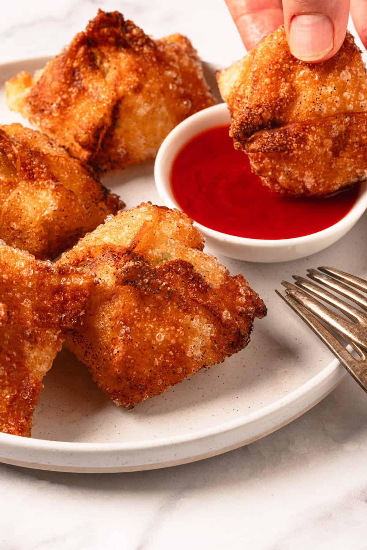 Crispy fried chicken bites with dipping sauce and fork on white plate.