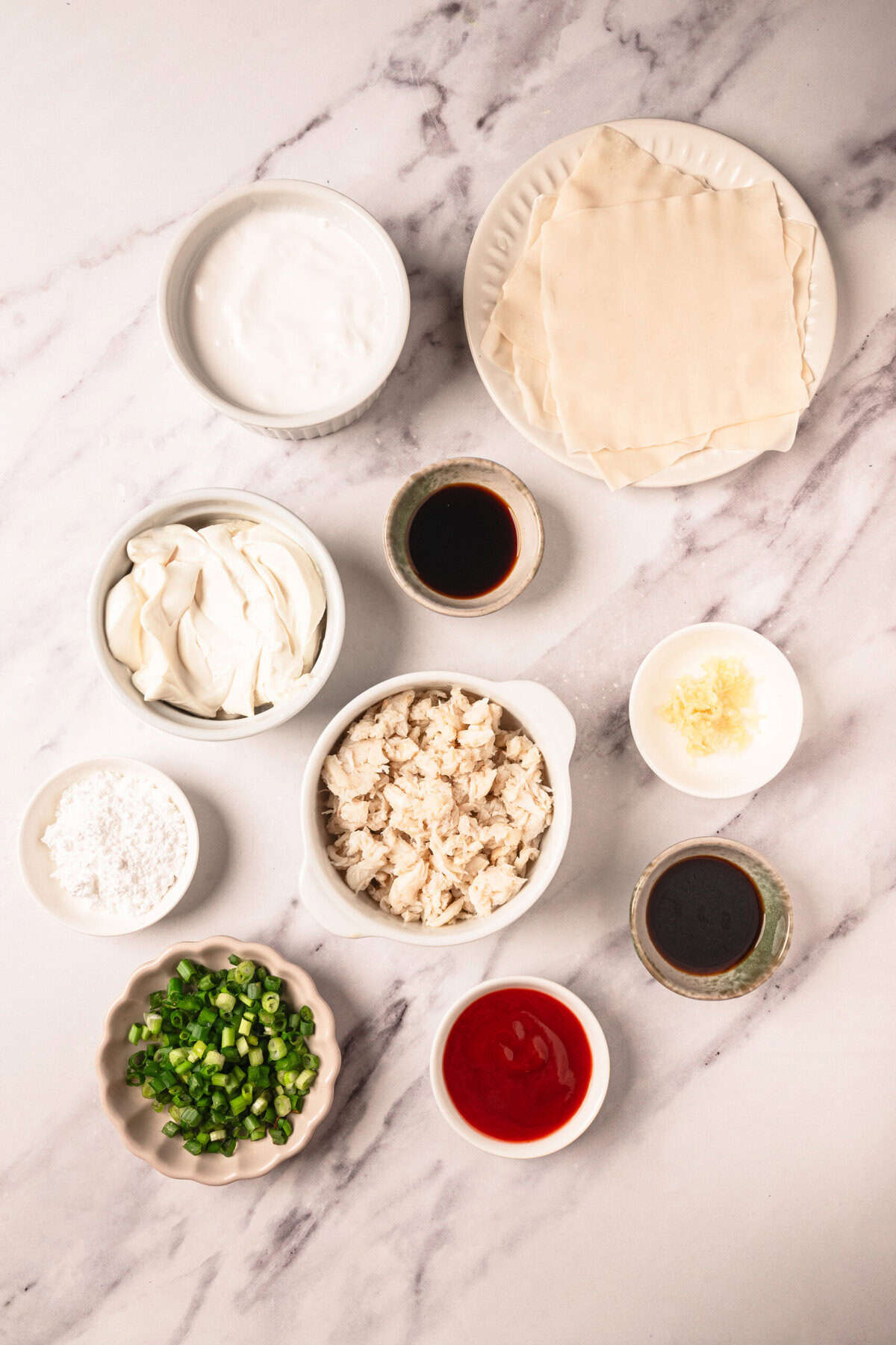 Mixed ingredients for crab rangoon appetizer, including crab meat, cream cheese, wonton wrappers, soy sauce, and green onions, on a white marble surface. Focuses on healthy and delicious appetizer recipes.