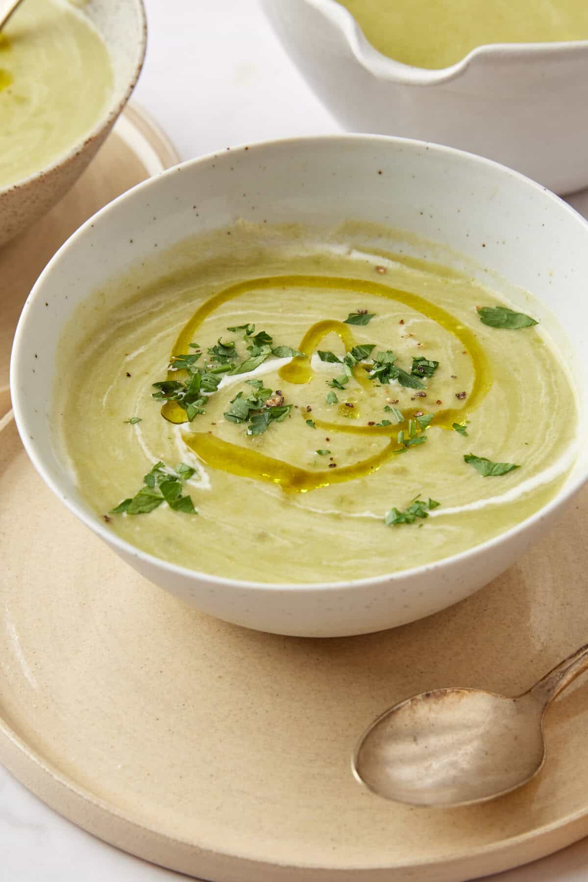 Creamy green vegetable soup garnished with fresh herbs and a drizzle of olive oil on a white bowl. Perfect for healthy eating and meal prep, packed with nutrients.
