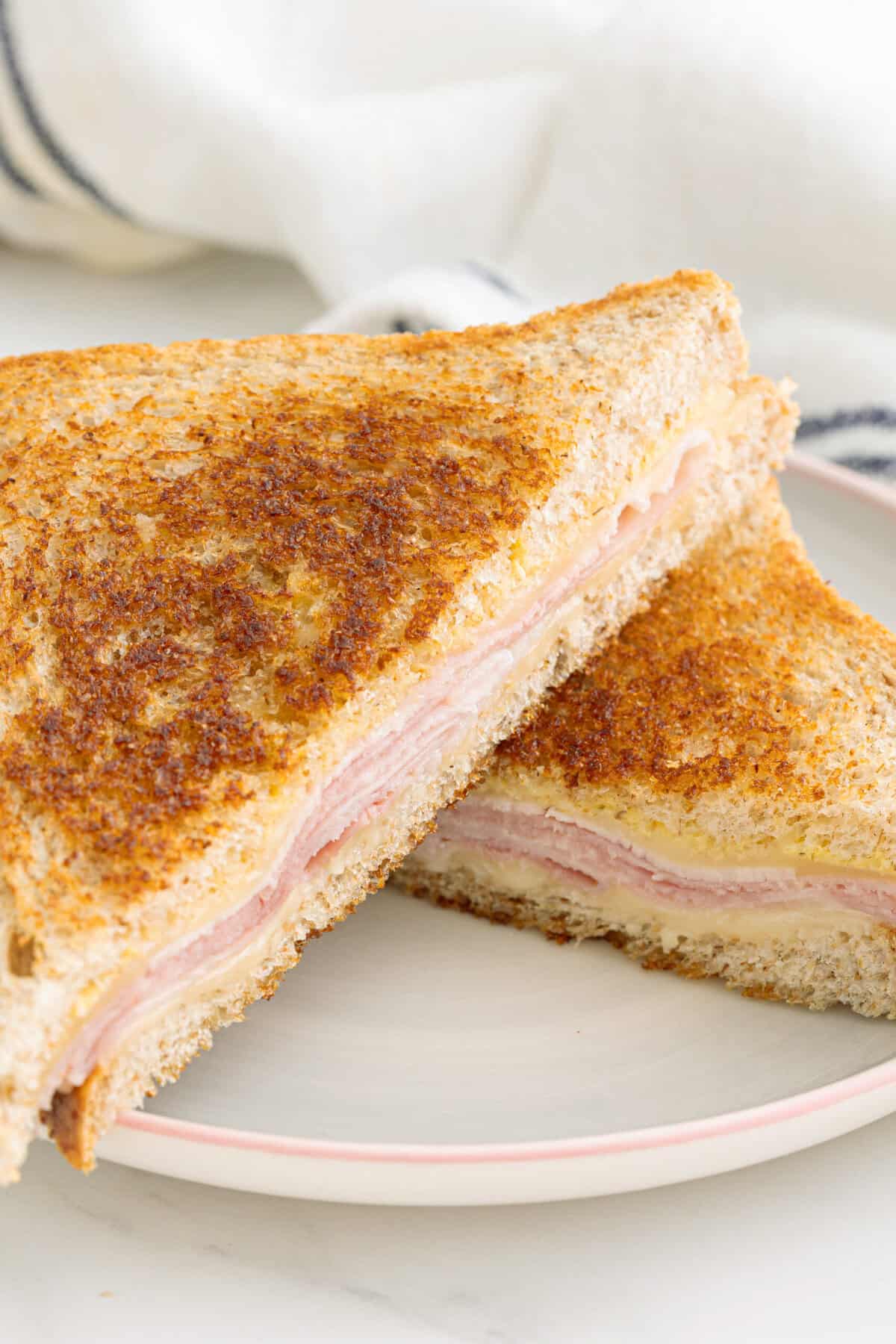 Crispy toasted sandwich with ham and molten cheese on whole grain bread, served on a white plate, emphasizing healthy and tasty food options from fitness faith.