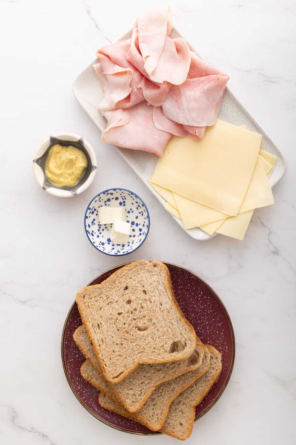 Slices of whole grain bread, slices of meat, cheese, butter and mustard on white marble surface - healthy and balanced food options for nutritious food.
