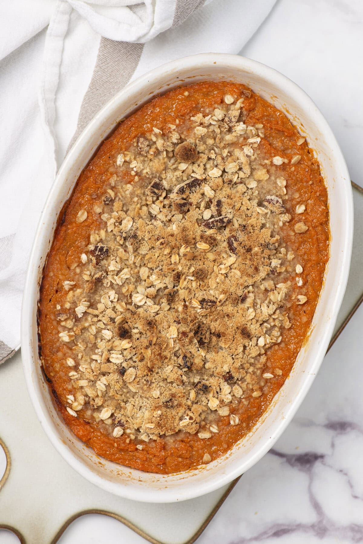 Oatmeal breakfast casserole topped with crunchy oats and nuts in a white baking dish, healthy meal recipe for weight loss and nutritious eating.