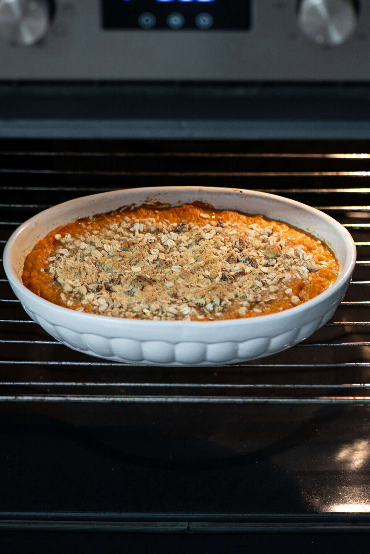 Baked sweet potato casserole with oatmeal topping in a white baking dish on a stove.