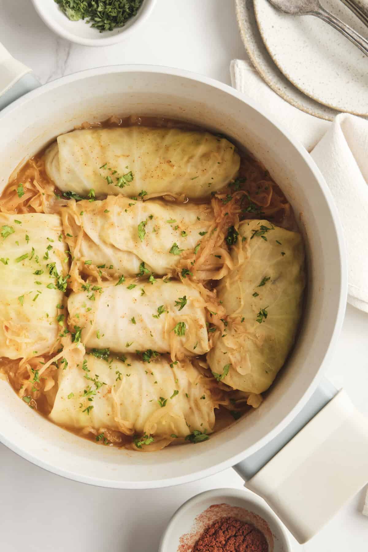 Succulent stuffed cabbage rolls in a white baking dish topped with fresh parsley, featuring healthy comfort food recipes from Food Faith Fitness.