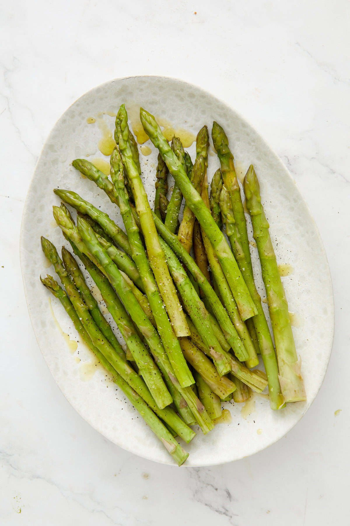 Fresh roasted asparagus spears drizzled with olive oil, seasoned with sea salt and black pepper, served on a white ceramic platter for healthy eating and nutrition.