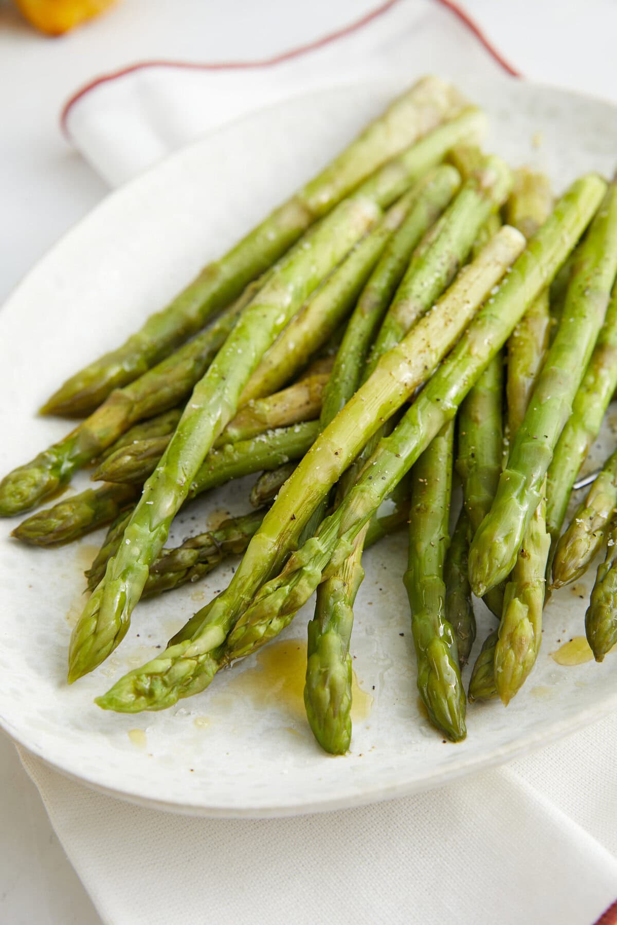 Fresh roasted asparagus spears drizzled with olive oil, seasoned with salt and pepper, on a white plate. Perfect for a healthy, low-calorie meal or side dish.