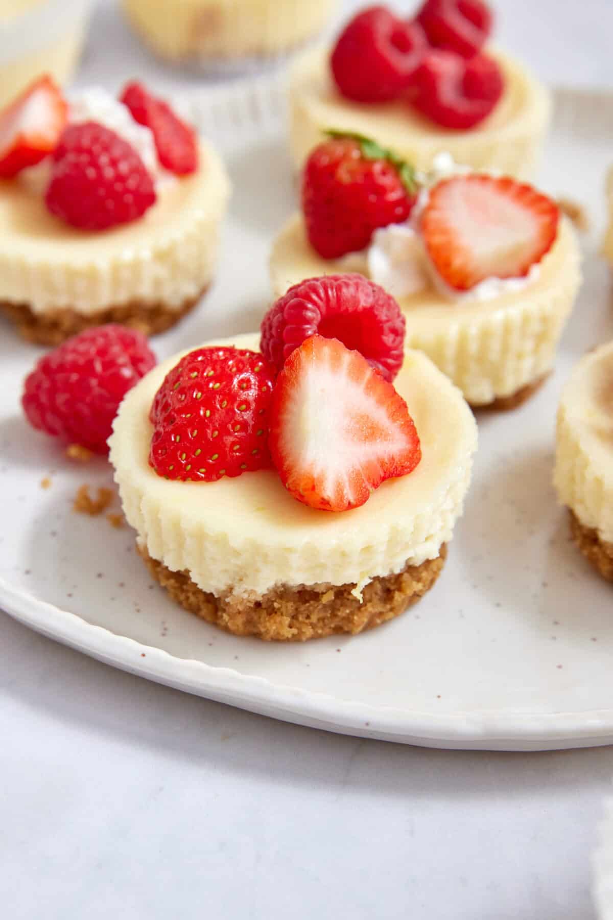 Fresh strawberry cheesecake bites topped with strawberries, raspberries, and whipped cream on a white plate. Perfect for healthy dessert ideas, fruit-based recipes, or elegant summer treats.