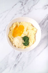 Mixing mashed potatoes with egg yolks, Parmesan cheese, and parsley for potato croquettes.