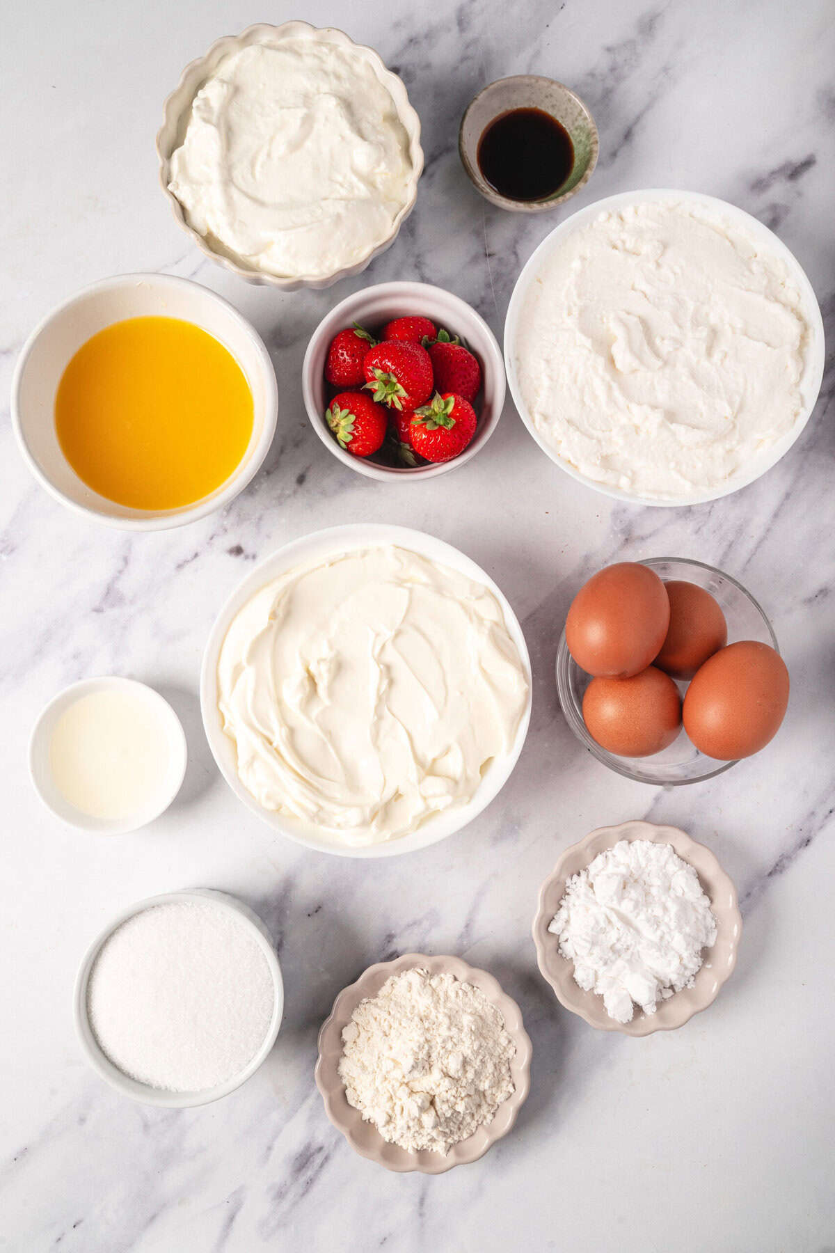 Fresh ingredients for strawberry shortcake, including strawberries, eggs, flour, sugar, vanilla, whipped cream, milk, and balsamic vinegar, arranged on a marble surface. Perfect for making a delicious dessert.