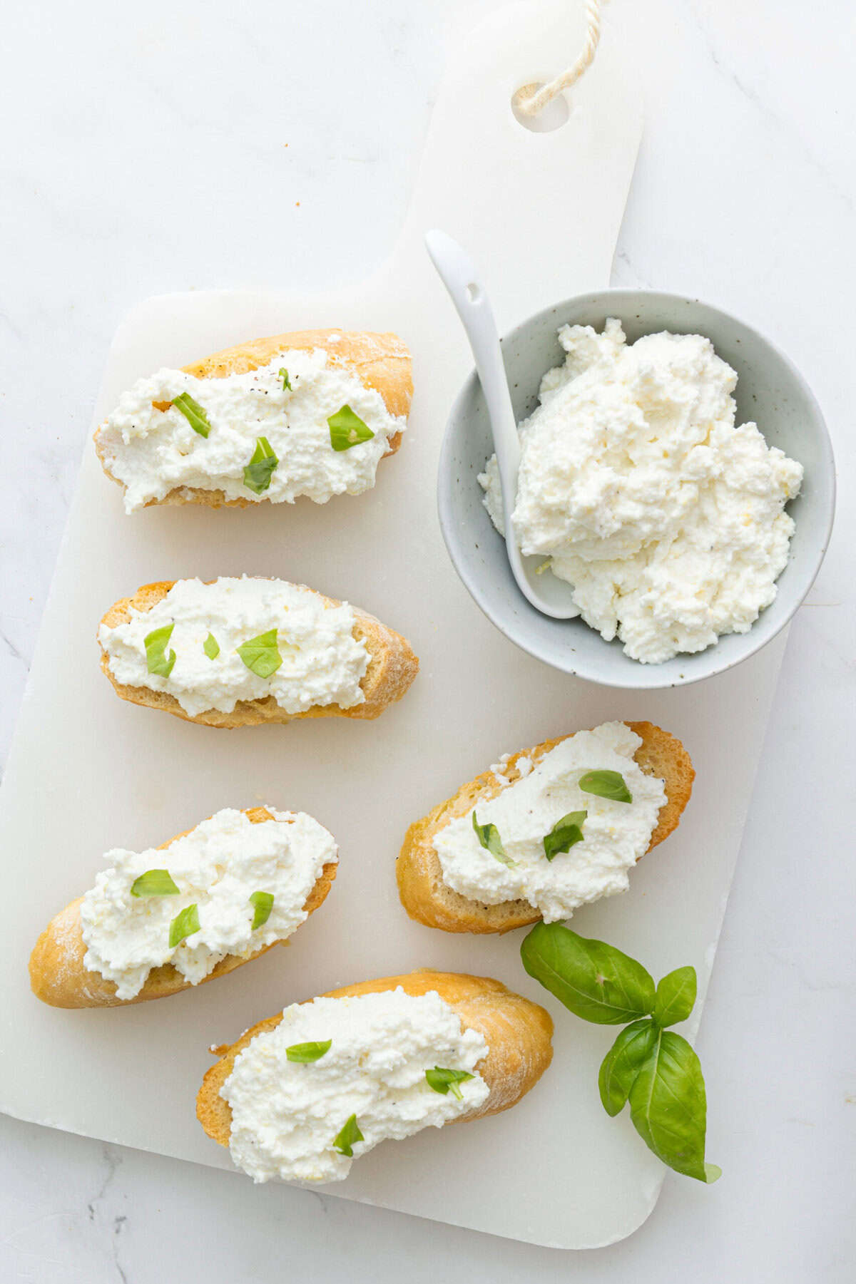 Cream cheese crostini appetizer topped with fresh basil on serving platter with ricotta cheese in bowl, healthy and delicious snack, perfect for entertaining or light meal, food faith fitness recipe.