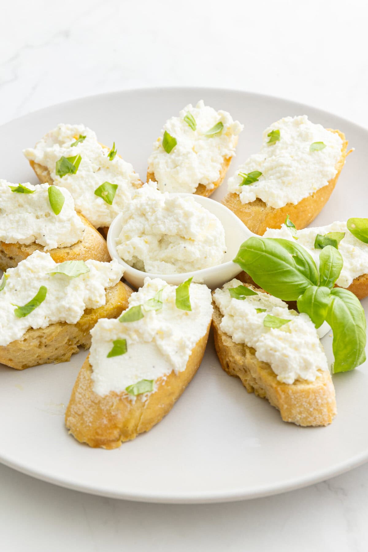 Creamy ricotta cheese spread on crispy toasted baguette slices garnished with fresh basil and green onion, perfect for healthy appetizers or snack ideas from Food Faith Fitness.