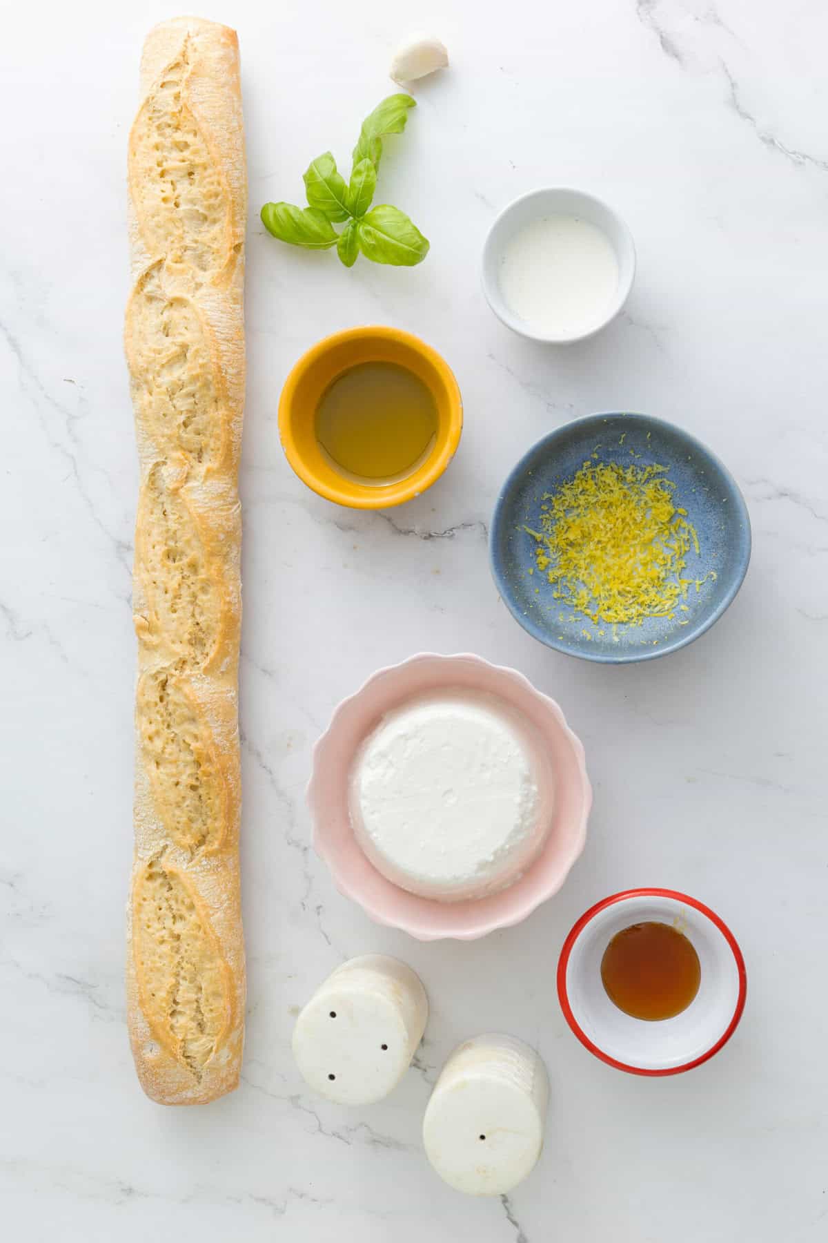 Fresh baguette bread and ingredients for a healthy Italian-style dish, including olive oil, garlic, lemon zest, milk, and herbs, promoting nutritious eating and clean eating recipes.