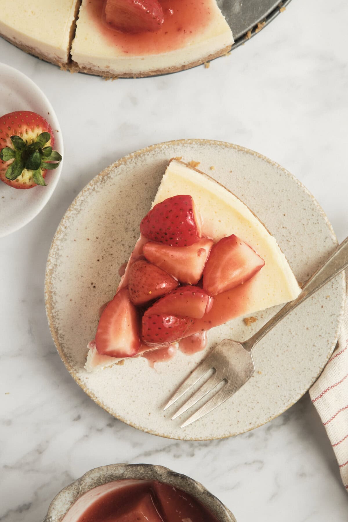 Fresh strawberry-topped cheesecake with a graham cracker crust, served on a neutral ceramic plate for a delicious healthy dessert option.