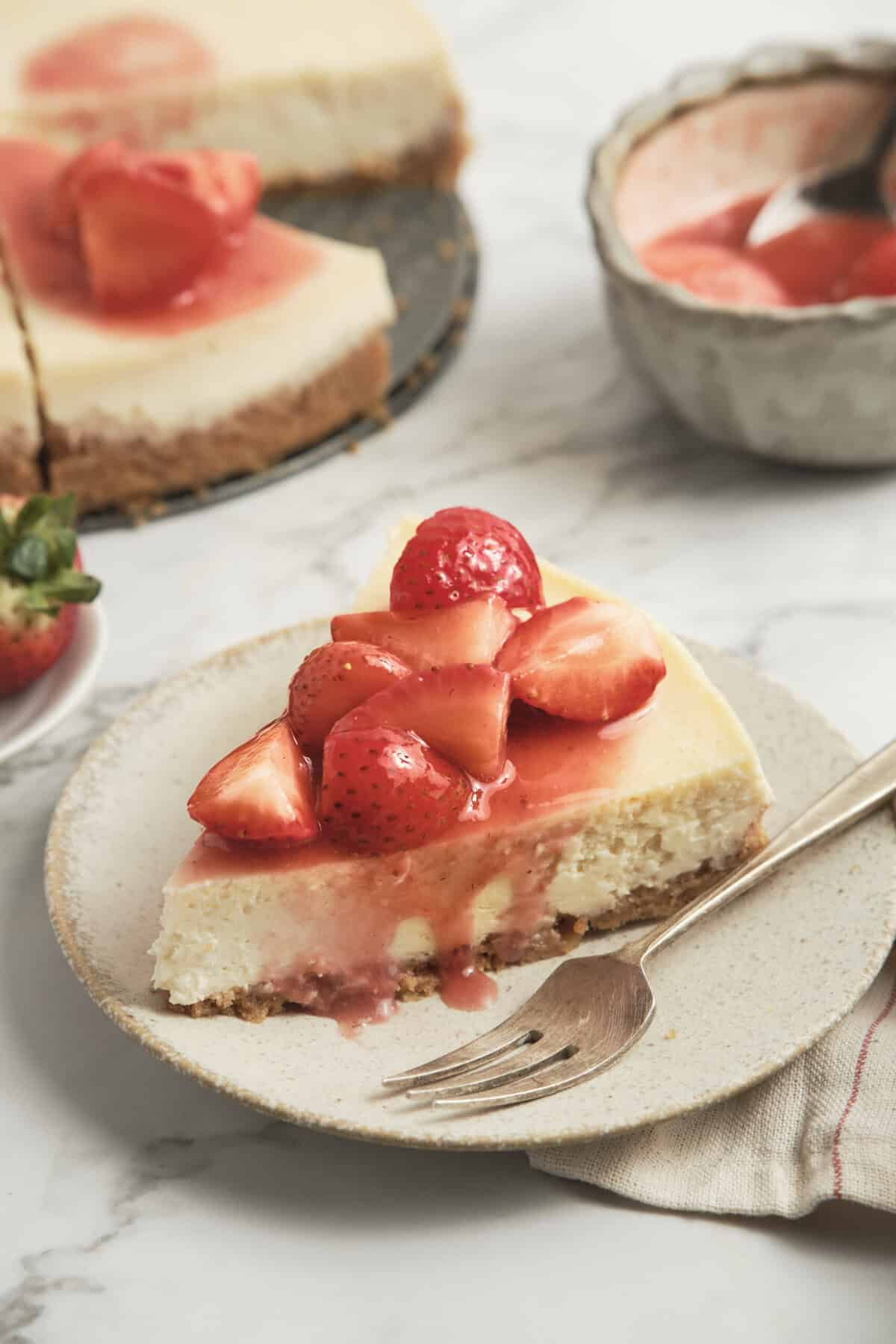 Fresh strawberry cheesecake slice with a graham cracker crust and strawberry sauce on top, served on a white plate. Perfect for healthy desserts and guilt-free treats from Food Faith Fitness.