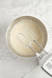 Beating the creamy filling for strawberry cheesecake in a metal bowl with an electric mixer.