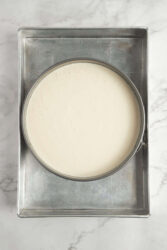 Creamy homemade cheesecake batter in a springform pan on a baking tray.