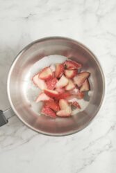 Combining quartered strawberries and sugar in a small saucepan for strawberry cheesecake topping.
