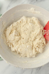 Stiff, shaggy sourdough bagel dough forming in a white bowl.