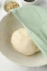 Sourdough bagel dough resting in a bowl, covered by a green towel.