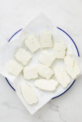 Slices of halloumi cheese being patted dry with a paper towel.