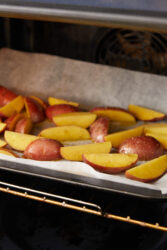 Seasoned potato wedges for chicken scarpariello roasting on a baking sheet in the oven.