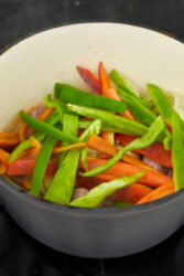 Saut&eacute;ing sliced bell peppers and onions in a pan for chicken scarpariello.