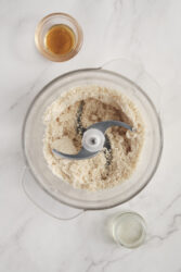 Adding honey to ground peanuts in a food processor for homemade peanut butter.