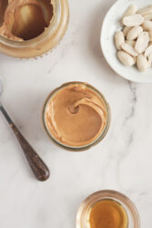 Homemade peanut butter in a jar with raw peanuts and honey.