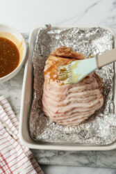 Brushing honey glaze onto a pre-sliced ham.