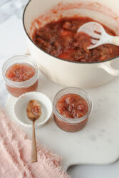 Homemade rhubarb jam in small glass jars on a white board.