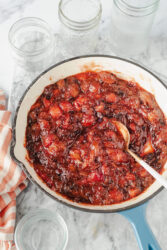 Strawberry-rhubarb jam simmering in a pan with empty jars nearby.