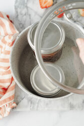 Jars of homemade strawberry-rhubarb jam being processed in a water bath.
