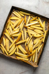 Seasoned potato slices on a baking sheet for cheeseburger fries.