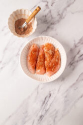 Sprinkling spice mix on raw chicken breasts for Chicken Lazone.