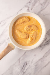Chicken Lazone cooking in a skillet with creamy sauce.