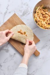 Folding a flour tortilla filled with shredded chicken and cheese to make chimichangas.