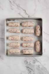 Raw ham croquettes shaped into logs on a baking sheet.