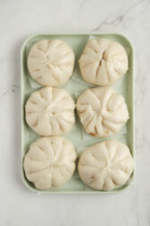 Six steamed pork buns on a light green tray.