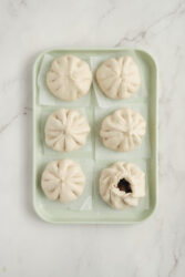 Gathering and pleating pork buns on a tray.